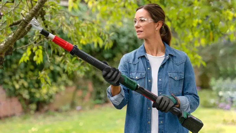 Eine Frau im Garten, die mit Hilfe der Akku-Astschere AdvancedPrune 18V-45 von Bosch einen Ast schneidet.